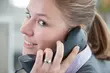 Smiling office worker holding a telephone handset while engaged in a conversation.